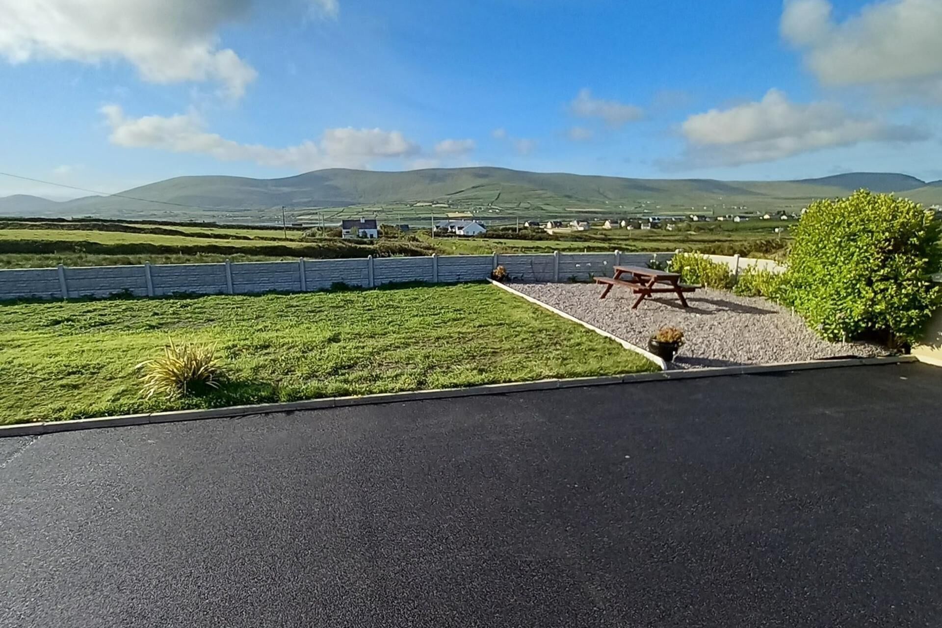 A parking area with a picnic table and a bench, surrounded by a grassy field and a stone wall.