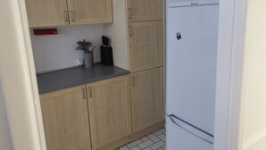 A kitchen with wooden cabinets, a countertop, a white refrigerator, and a red appliance on the left.