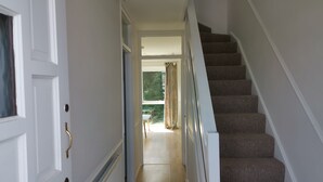 A hallway with a carpeted staircase, a white door, and a view of a balcony with curtains.
