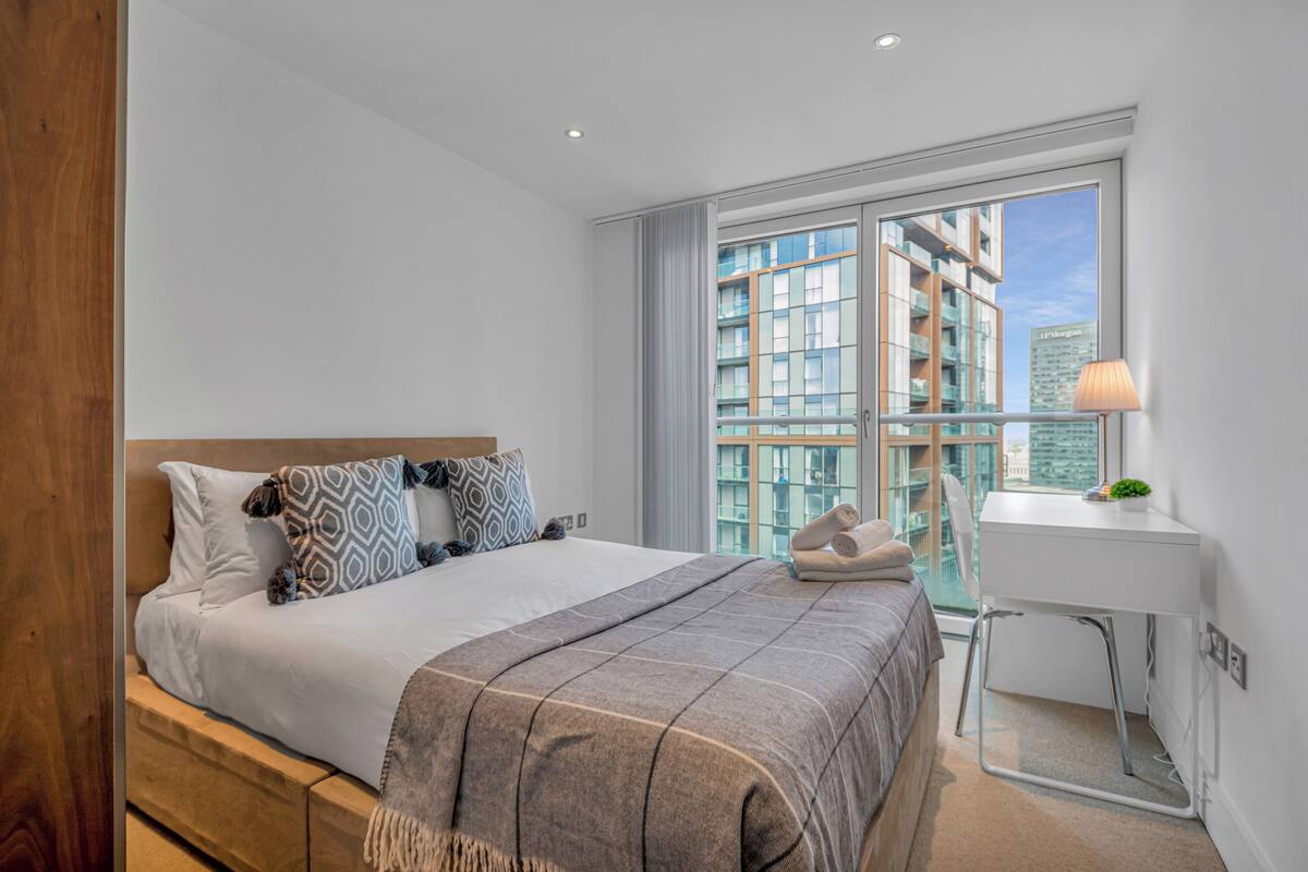 Une chambre d’hôtel moderne, dotée d’un grand lit, d’un bureau et offrant une vue sur le paysage urbain grâce à de grandes fenêtres.