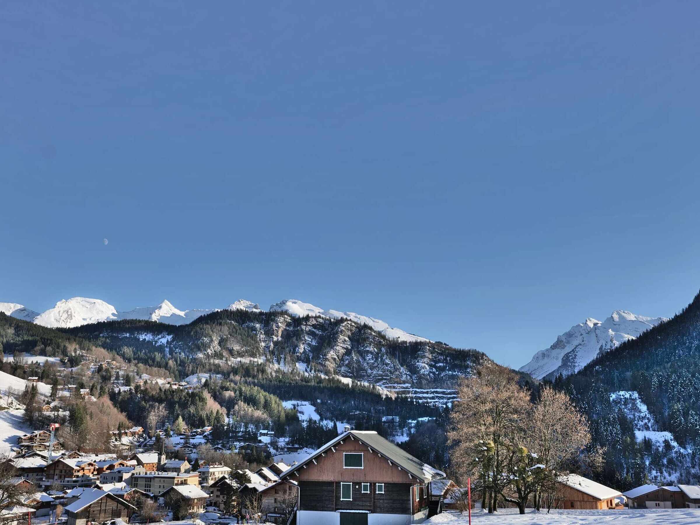 En by belägen i bergen, med snötäckta hus och en framträdande byggnad i trä som syns tydligt på bilden.