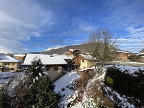 A snow-covered village with traditional wooden houses, a clear sky, and mountains in the background.