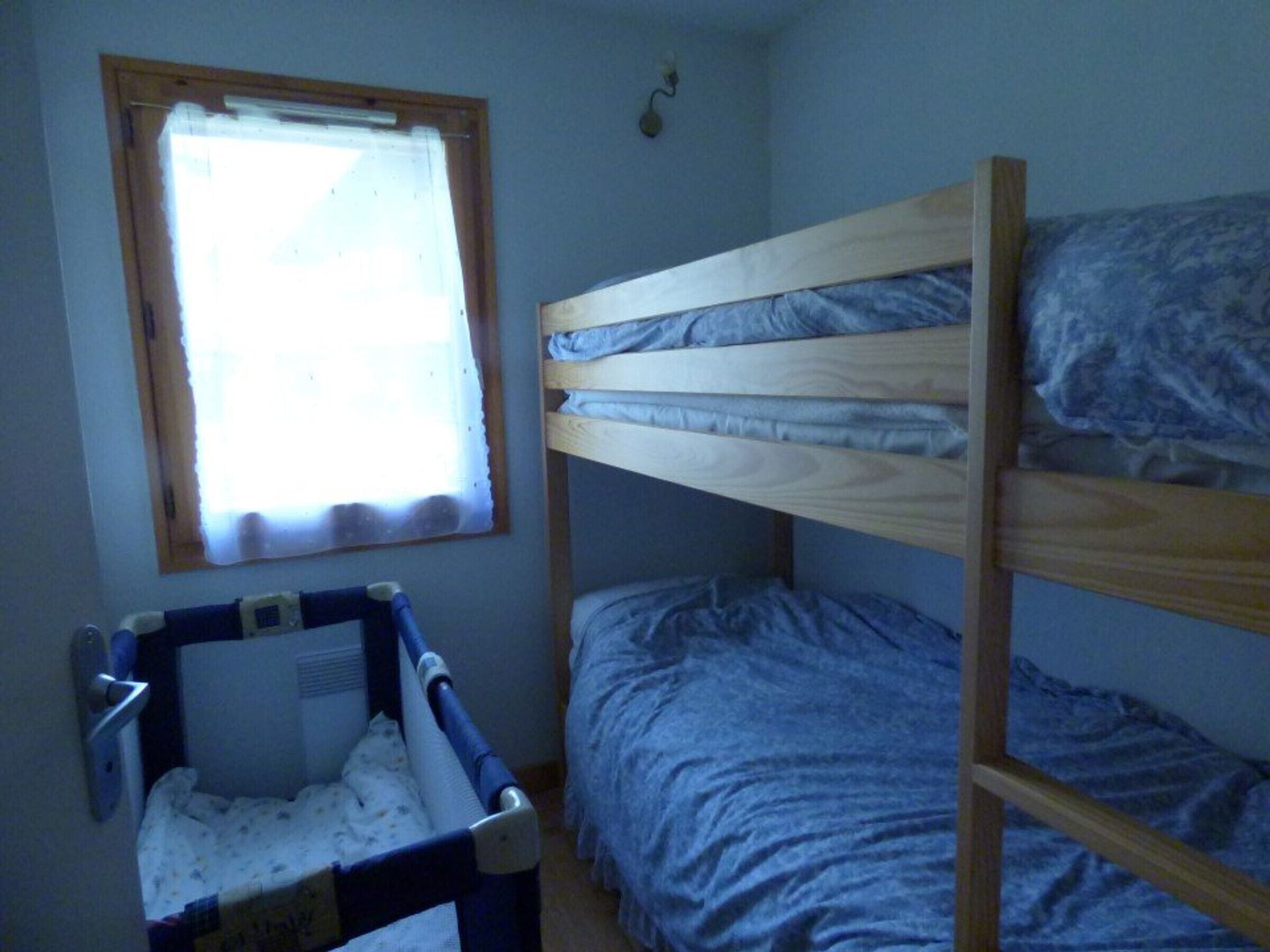 Une chambre avec un lit superposé, une fenêtre, un berceau et une porte.