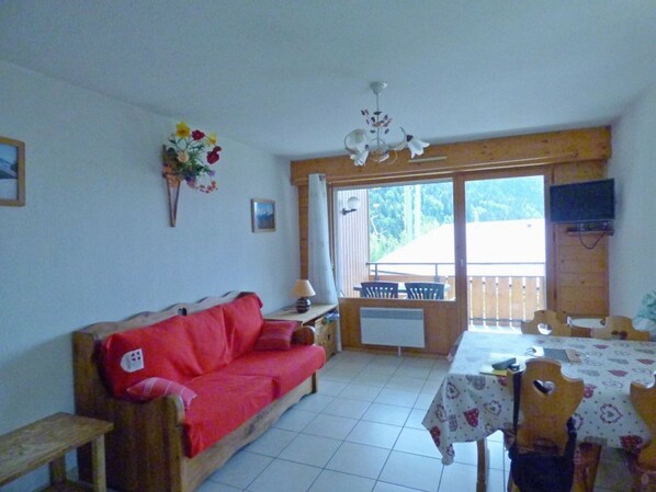 A cozy room with a red sofa, a dining table with chairs, a window with a view, and a ceiling fan.