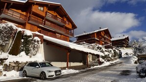 A wooden chalet with balconies, a car parked in front, and snow on the ground. - Mountain-Style Apartment for 6-7 Near Cable Cars and Town Center in Le Grand-Bornand (Le Grand-Bornand)