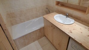 A small bathroom with a bathtub, a wooden vanity with a sink, and a mirror above the sink. - Mountain-Style Apartment for 6-7 Near Cable Cars and Town Center in Le Grand-Bornand (Le Grand-Bornand)