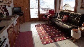 A cozy living room with a sofa, a red rug, and a wooden dining table. - Mountain-Style Apartment for 6-7 Near Cable Cars and Town Center in Le Grand-Bornand (Le Grand-Bornand)