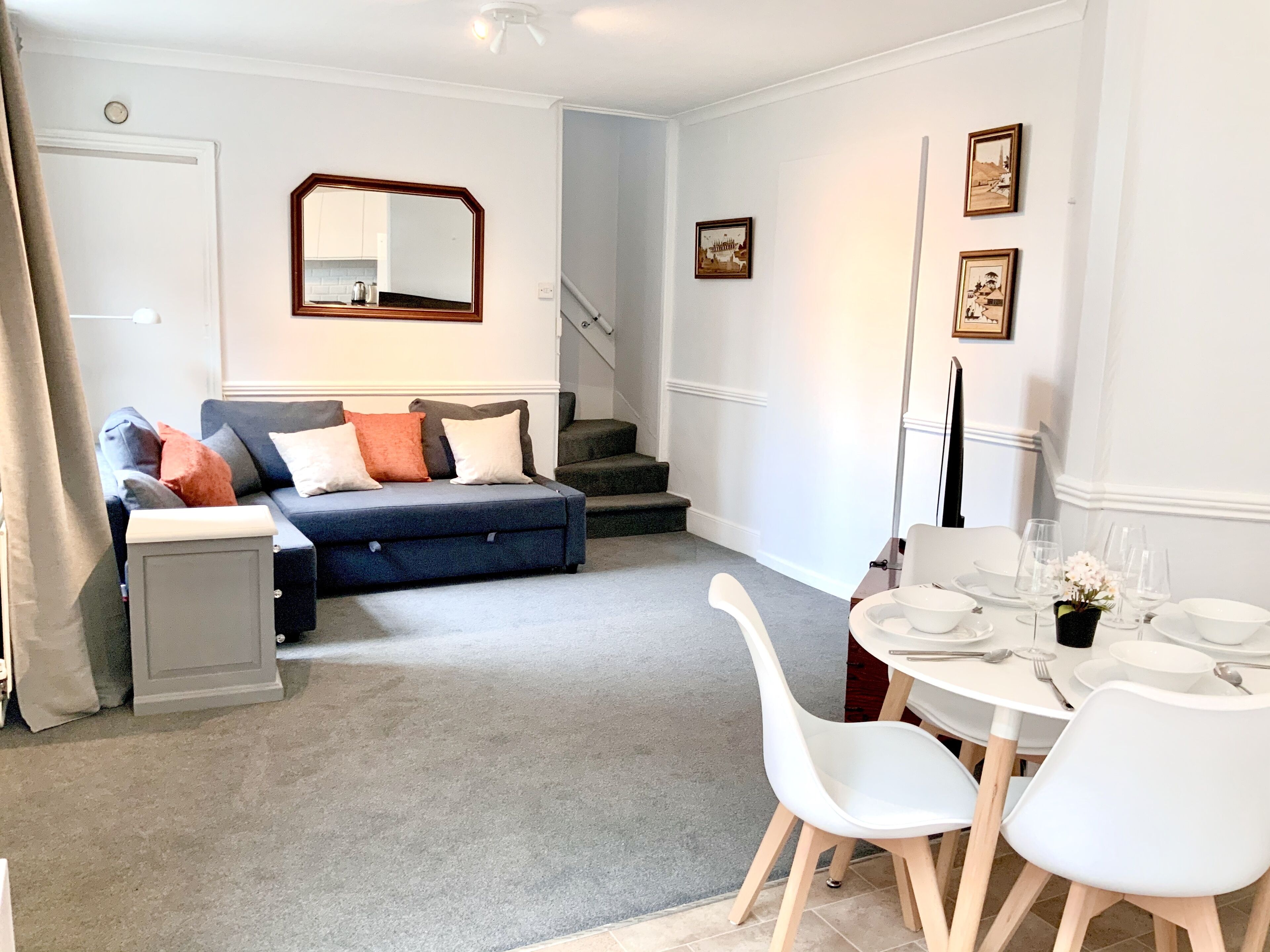 A modern living room with a blue sofa, white chairs, and a dining table set for six.
