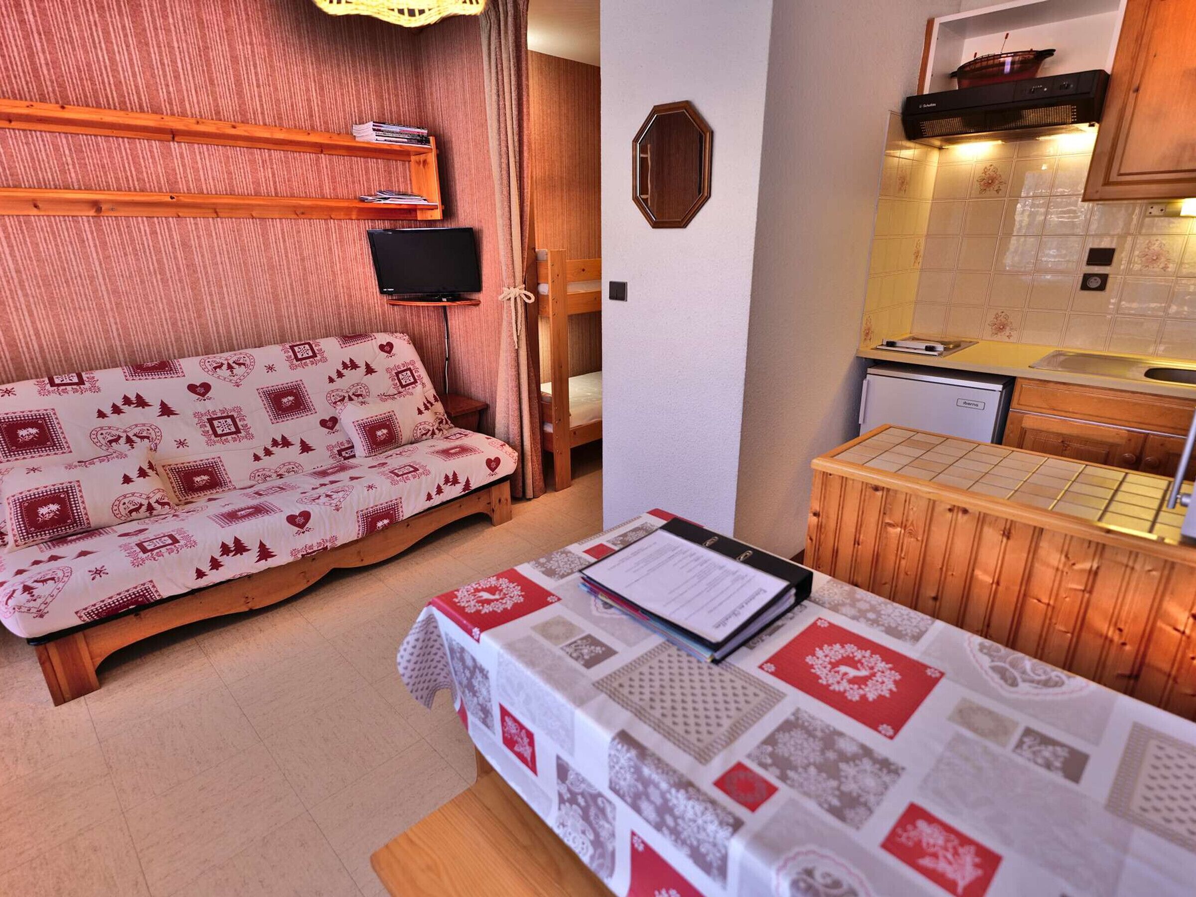 Una habitación acogedora con sofá, una mesa con carta, televisor y zona de cocina con fregadero y estufa.