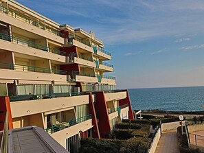 Um hotel com vários andares, varandas, vista para o mar e um caminho pavimentado.