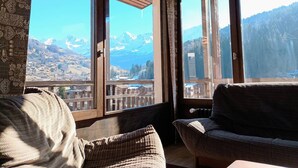 Une pièce dotée d’une grande fenêtre donnant sur les montagnes, de murs en bois et d’un coin salon confortable agrémenté d’un plaid à motifs.