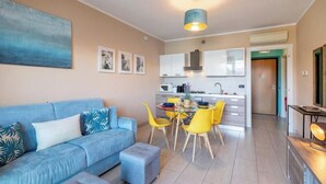 A modern living room with a blue sofa, a dining area with yellow chairs, and a kitchen with white cabinets. - FOREVER by Design Studio (Bellano)
