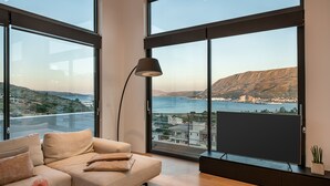 Un salon moderne doté d’une grande fenêtre donnant sur une ville côtière et des collines.