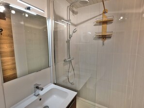 Een moderne badkamer met een douchecabine van glas, een witte wastafel en een houten wastafelmeubel.