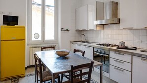 Eine Küche mit weißen Schränken, einem gelben Kühlschrank, einem Esstisch mit Stühlen und einem Fenster mit Jalousien.