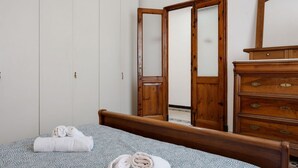 Ein Schlafzimmer mit einem Bett, einer Holzkommode, einem Kleiderschrank und einem Spiegel.