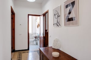 A hallway with a wooden floor, a white wall, and a door leading to a bathroom.