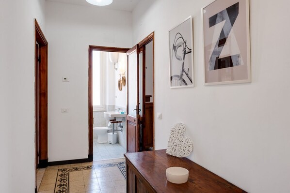 A hallway with a wooden floor, a white wall, and a door leading to a bathroom.