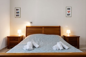 A neatly made bed with a patterned bedspread, two bedside lamps, and two rolled towels on the bed.