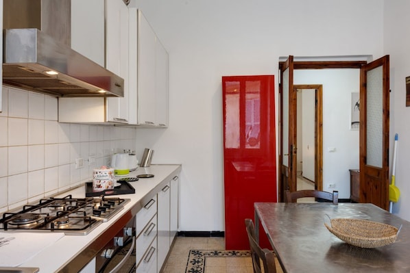 A kitchen with a gas stove, white cabinets, a red door, and a dining table with a basket.