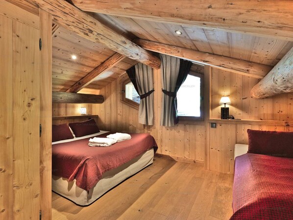 A cozy wooden cabin bedroom with a bed, a nightstand, and a window with curtains.