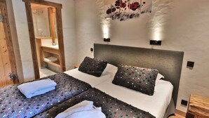 A bedroom with two beds, a wooden ceiling, a wall-mounted artwork, and a wooden door.