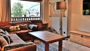 A cozy living room with a sofa, a wooden table, and a large window offering a view of the outdoors.