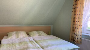 En säng för en person med en sänggavel i trä, i ett rum med ett sluttande tak.
