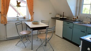 Ett kök med ett matbord, stolar, en diskho och ett fönster med gardiner.