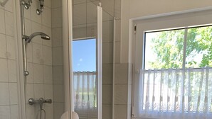 Ett badrum med en dusch som är avskärmad med glasväggar, en toalett och ett fönster med utsikt över grönområden.