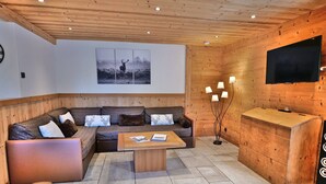 A cozy living room with a wooden ceiling, a large sofa, a coffee table, and a TV mounted on the wall. - Charming 3-room renovated with sauna and jacuzzi for 6 in Grand-Bornand (Le Grand-Bornand)