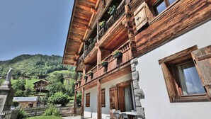 A traditional wooden chalet with balconies, stone pillars, and a stone wall. - Charming 3-room renovated with sauna and jacuzzi for 6 in Grand-Bornand (Le Grand-Bornand)