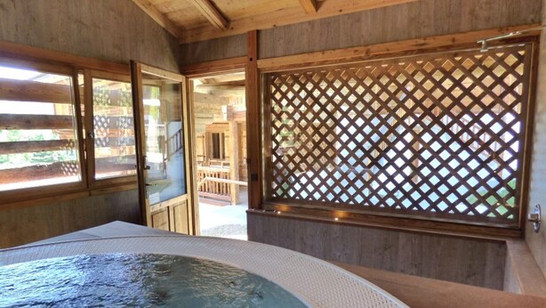 A wooden room with a hot tub, a lattice screen, and a view of a wooden deck outside. - Charming 3-room renovated with sauna and jacuzzi for 6 in Grand-Bornand (Le Grand-Bornand)