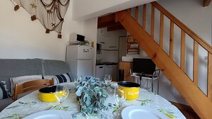 Een eetgedeelte met een ronde tafel gedekt voor twee personen, een bankstel op de achtergrond en een trap naar de bovenverdieping.