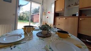 Een eetruimte met een tafel gedekt voor twee personen, een kamerplant en uitzicht op de achtertuin door een open deur.