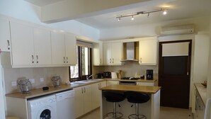 Cocina compacta con armarios blancos, lavadora, cafetera y dos taburetes.