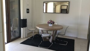 Un pequeño comedor con una mesa redonda, dos sillas, un florero y un espejo en la pared.