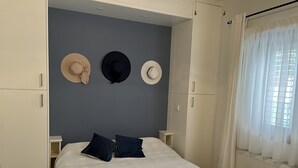 Un dormitorio con una cama, dos mesitas de noche, un armario y una pared decorada con tres sombreros.