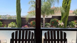 Mesa servida con platos, cubiertos y dos calabazas verdes, con vista a un jardín con árboles altos y cielo despejado.