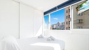 A modern hotel room with a large bed, a view of a cityscape through a window, and a flat-screen TV mounted on the wall. - Don Paco 12-B Deluxe Apartment Levante Beach (Benidorm)