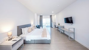 A modern hotel room with a large bed, bedside tables, a desk, a flat-screen TV, and a view of the city through large windows. - GRAND PA Hotel&Resort Lamphun Chiang Mai (Lamphun)