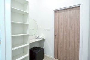 Una habitación con paredes blancas, una puerta de madera, un espejo y un caja de almacenamiento negra.