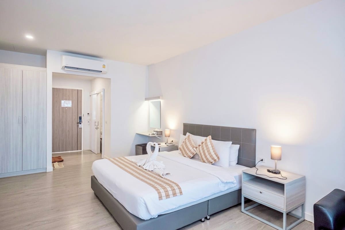 A modern hotel room with a large bed, bedside tables, a wardrobe, and an air conditioning unit.