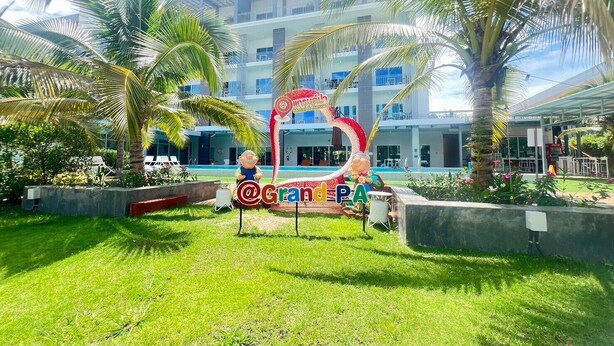 A hotel entrance with palm trees, a sign for @GrandPA, and a pool in the background. - GRAND PA Hotel&Resort Lamphun Chiang Mai (Lamphun)