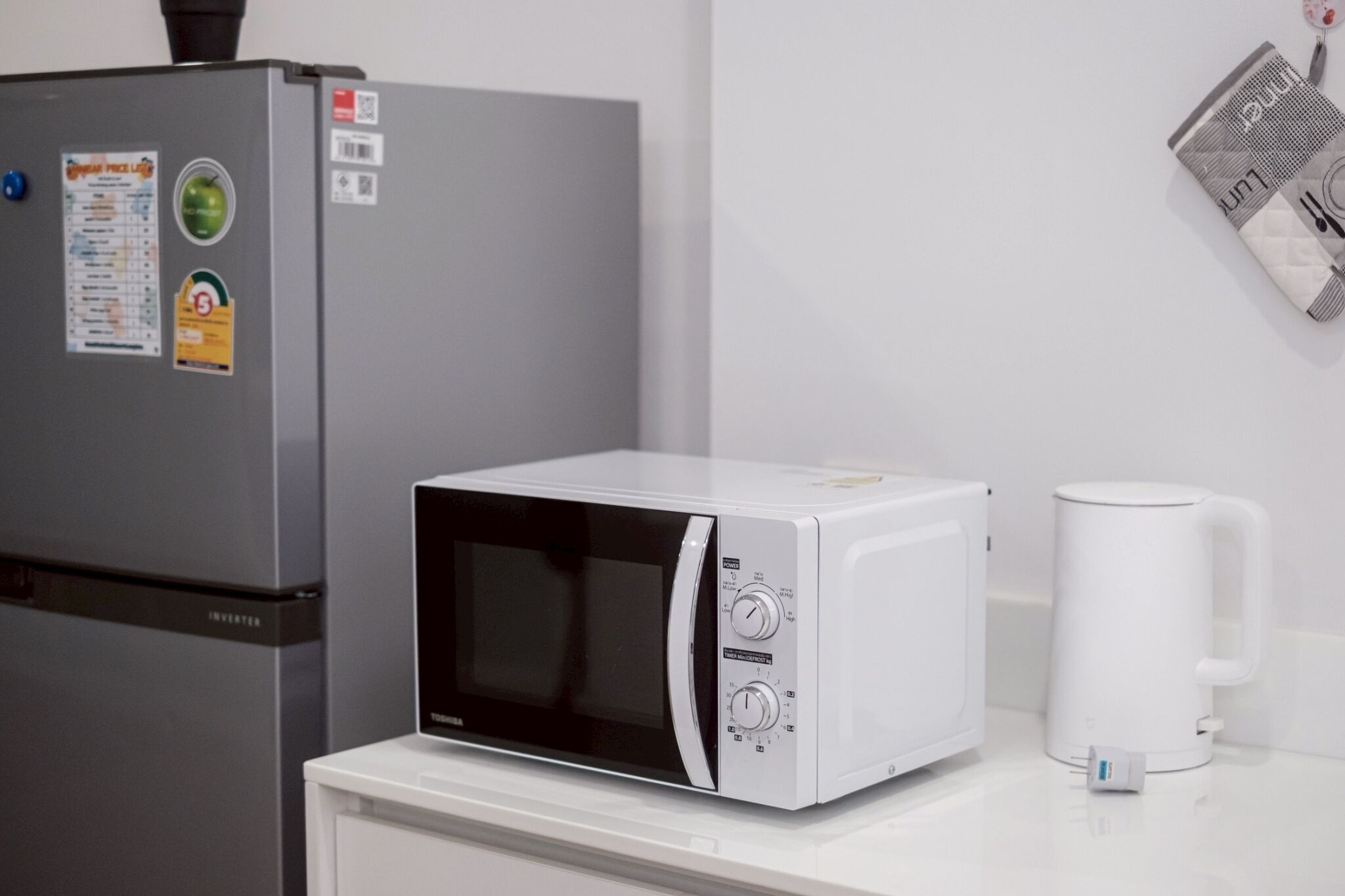 A kitchen with a microwave, a kettle, and a refrigerator.