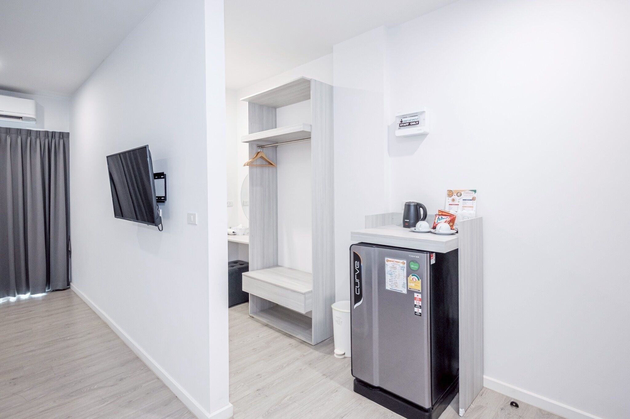 Una habitación de hotel moderna con refrigerador, televisor de pantalla plana, kitchenette y vestidor.