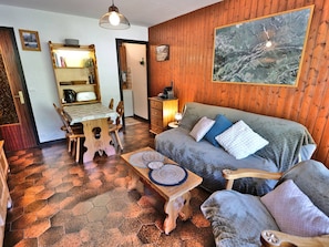 A cozy room with a wooden wall, a sofa with cushions, a wooden dining table with chairs, and a coffee machine.