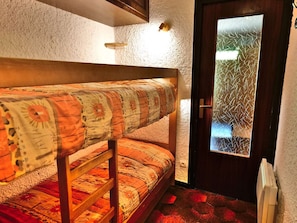 A bunk bed with patterned bedding, a door with frosted glass, and a radiator.