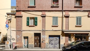 A building with a brick facade, green shutters, and a mural on the lower wall. - A pochi passi da Piazza Maggiore by Wonderful Italy (Bologna)