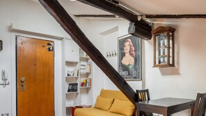 A room with a wooden door, a yellow sofa, a dining table with chairs, a bookshelf, and a poster on the wall.